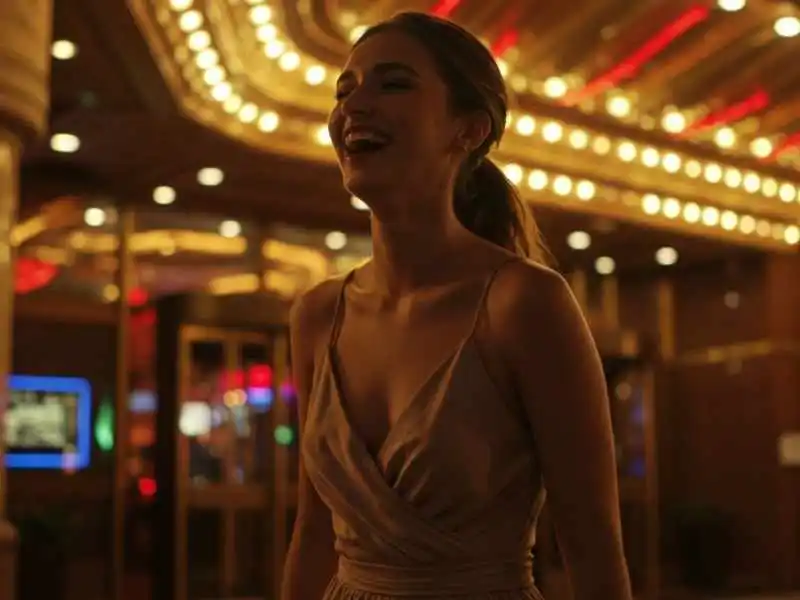 Happy woman in a dress smiling outside a brightly lit casino at night
